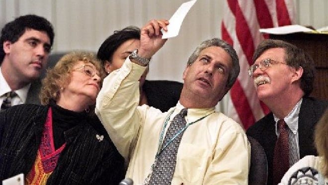 Some of the major players during the 2000 election recount in West Palm Beach included John Bolton (right), seen here examining a ballot held by Palm Beach County Canvassing Board Chairman Charles Burton.