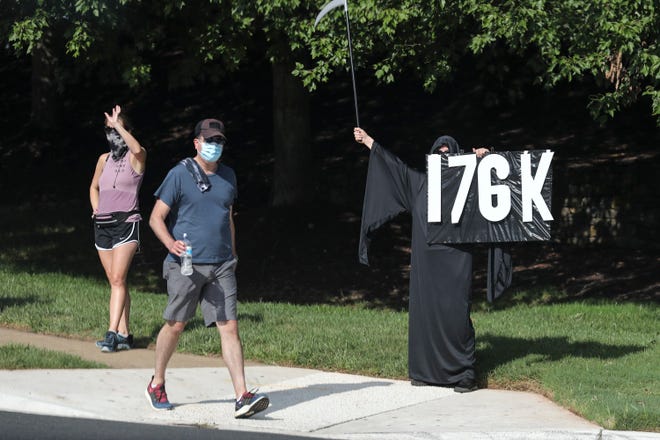 A protester holds a sign referencing the coronavirus death toll in the U.S. as President Donald Trump's motorcade arrives at Trump National Golf Club in Sterling, Va., on Sunday. (Oliver Contreras/The New York Times)