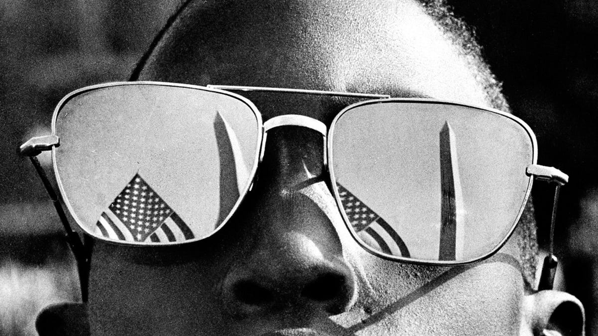 The top of the Washington Monument and part of a U.S. flag are reflected in the sunglasses of Austin Clinton Brown, 9, of Gainesville, Ga., as he poses at the Capitol where he joins others in the March on Washington on Aug. 29, 1963.