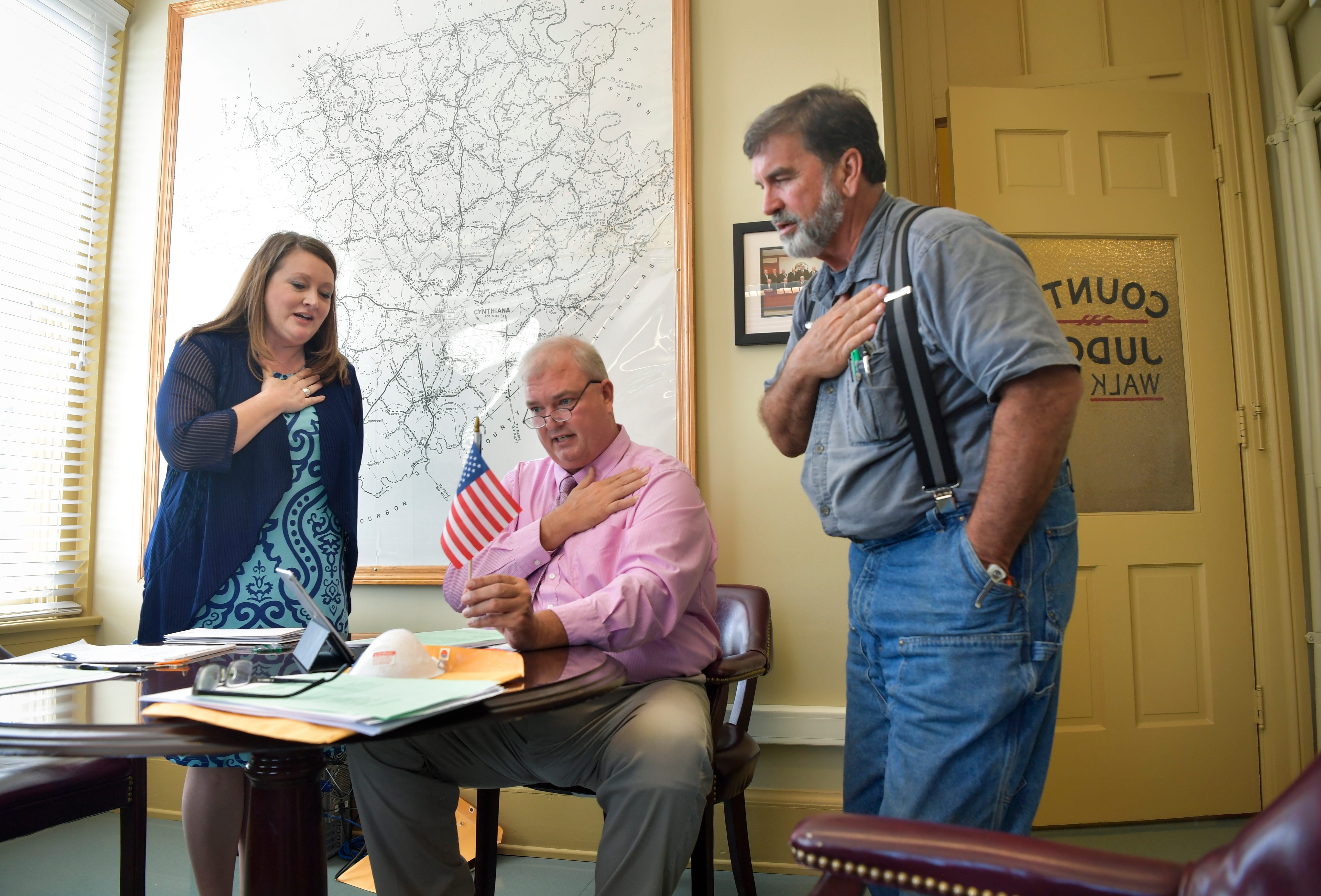 Harrison County Judge Alex Barnett, center, recites the Pledge of Allegiance before a virtual meeting of court magistrates in Cynthiana, Ky. Joining him are Treasurer Melody McClure and 7th District Magistrate Dwayne Florence.