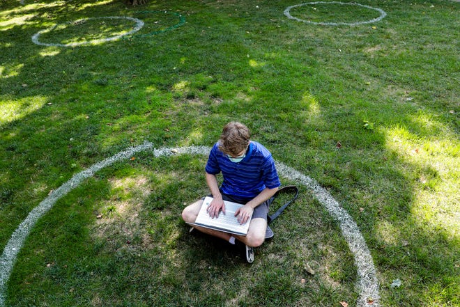 FILE - In this Aug. 25, 2020, file photo, Logan Armstrong, a junior, works while sitting inside a painted circle on the lawn of the Oval during the first day of fall classes at Ohio State University in Columbus, Ohio. Officials in college towns all over the U.S. are fretting that off-campus students are being counted in places other than the communities where their schools are located.  (Joshua A. Bickel/The Columbus Dispatch via AP, File)