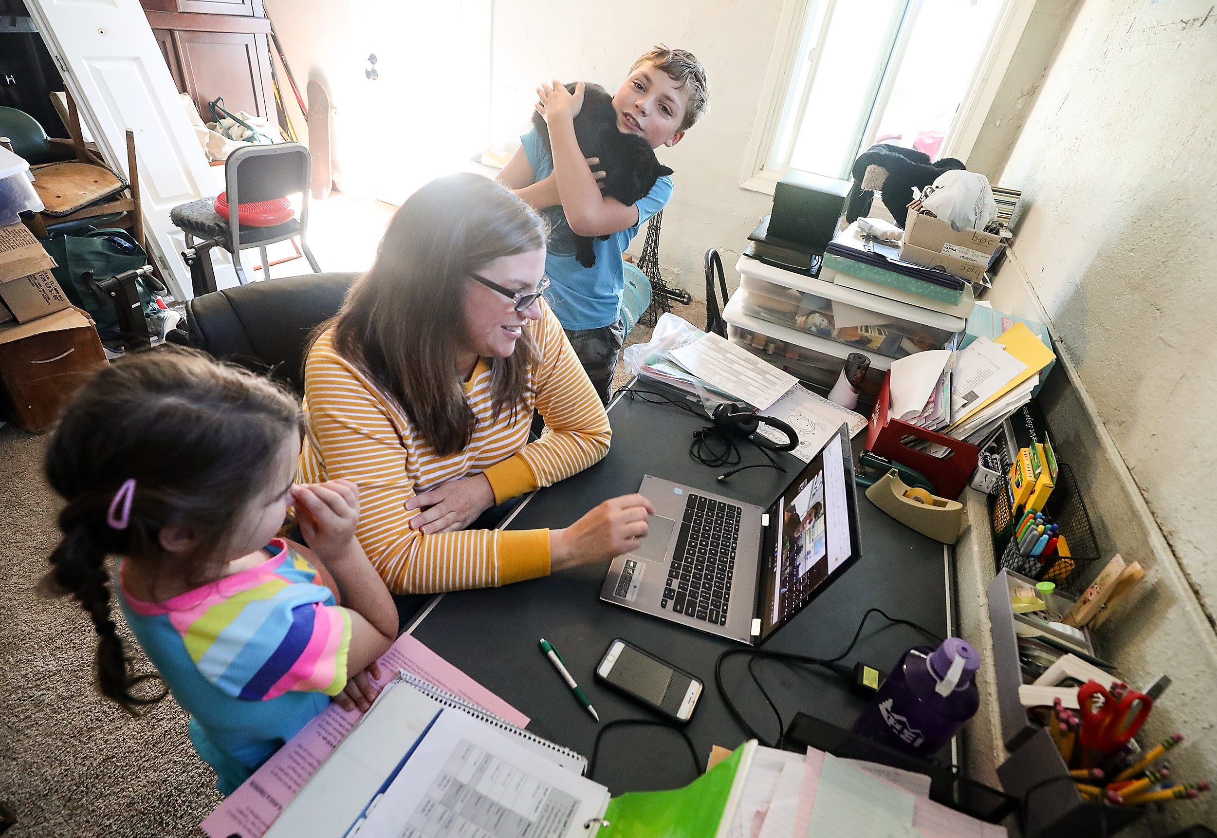 Mountain View Middle School teacher Anne Pedelaborde watches a video of one of her students introducing themselves as son Alex and daughter Emma gather around her desk in the basement of the family's home in Bremerton, Wash. on Wednesday, Sept. 2, 2020.