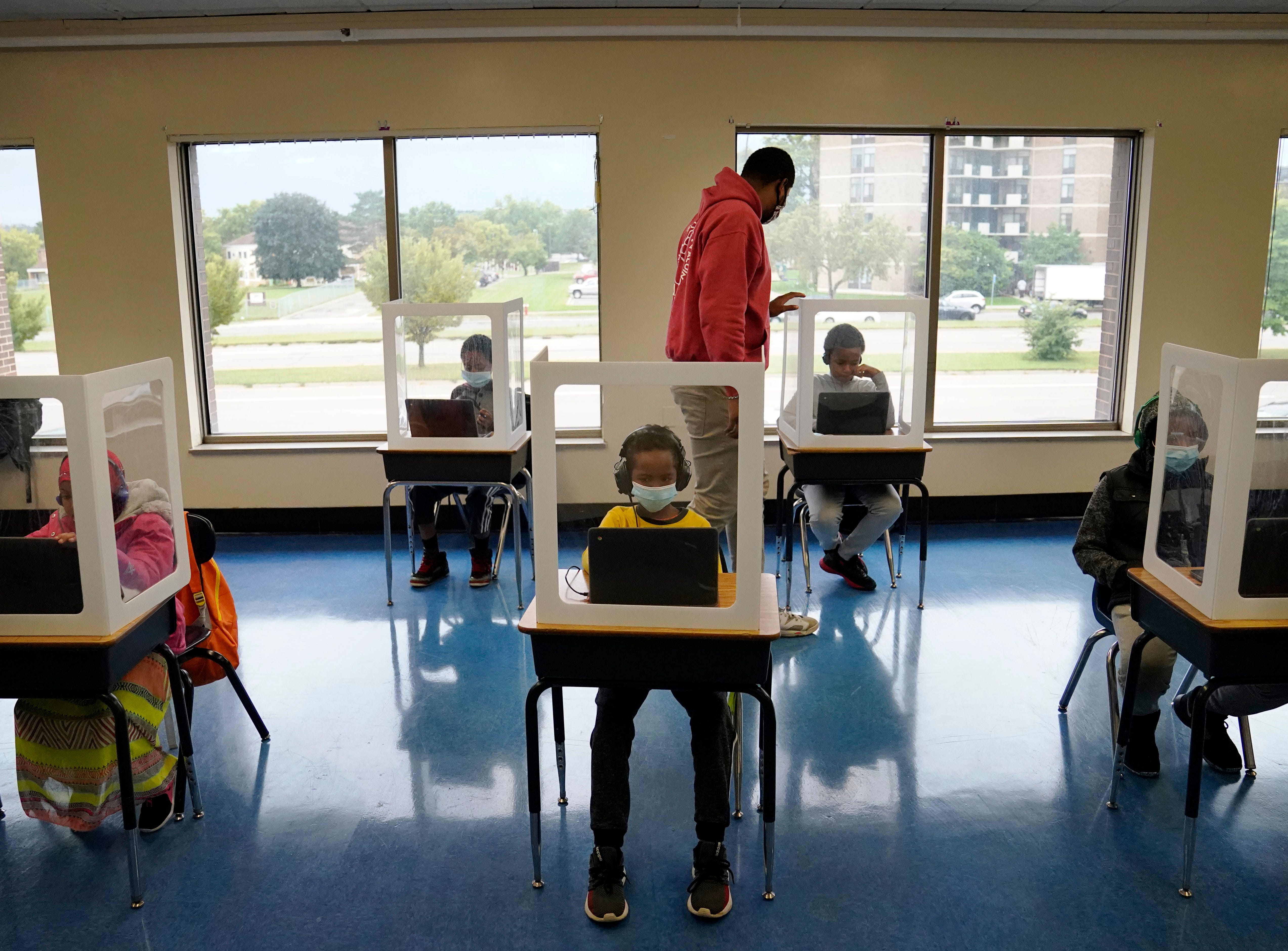 Paraprofessional Jaevon Walton, center, reminds a student to wear his face mask in a learning pod of second through seventh graders.