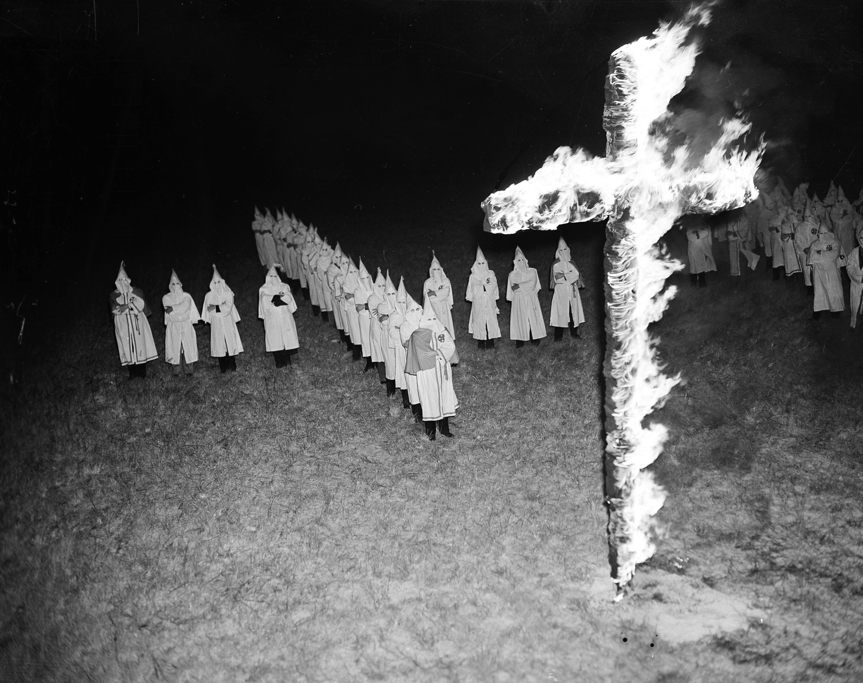 Members of the Ku Klux Klan, wearing traditional white hoods and robes, stand back and watch with their arms crossed after burning a 15-foot cross in Tampa on Jan. 30, 1939.