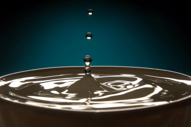 A studio photo of water drops into a cup.
