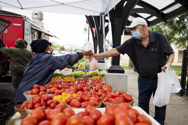 Mai Xiong, left, hands fresh vegetables to a customer Friday, Sept. 11, 2020, at Cameron Park Farmers Market in La Crosse.