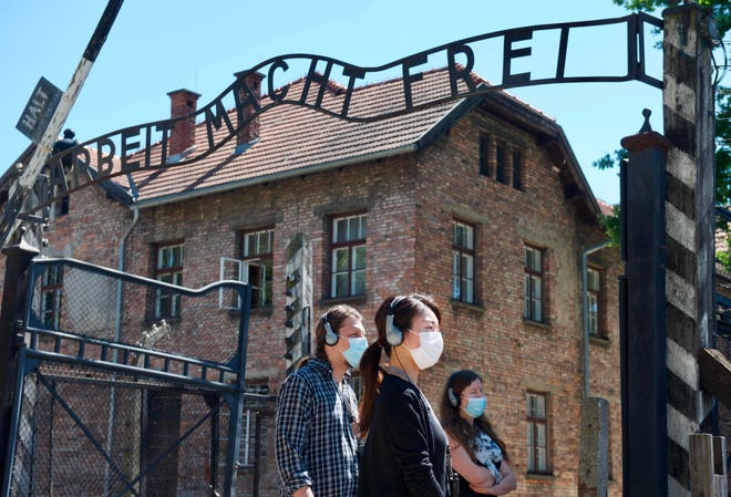 Visitors are seen near the gate with its inscription "Work sets you free" as the memorial site of the former German Nazi death camp Auschwitz in Oswiecim reopens on July 1, 2020 to visitors, for the first time after a break caused by novel coronavirus COVID-19 lockdown.