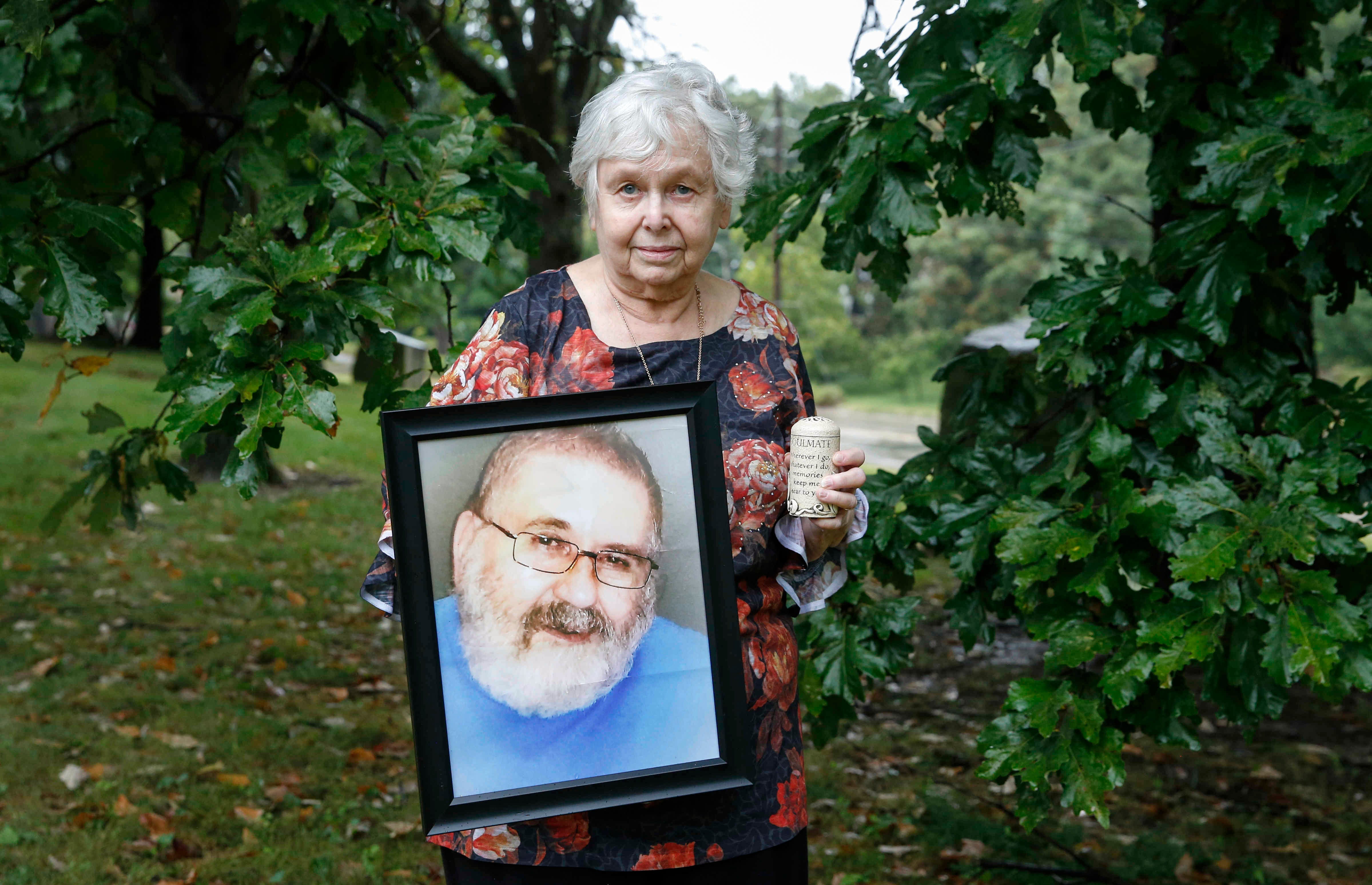 Jan Baxa poses for a photo with a portrait of her husband Ken Baxa, who died from COVID-19.