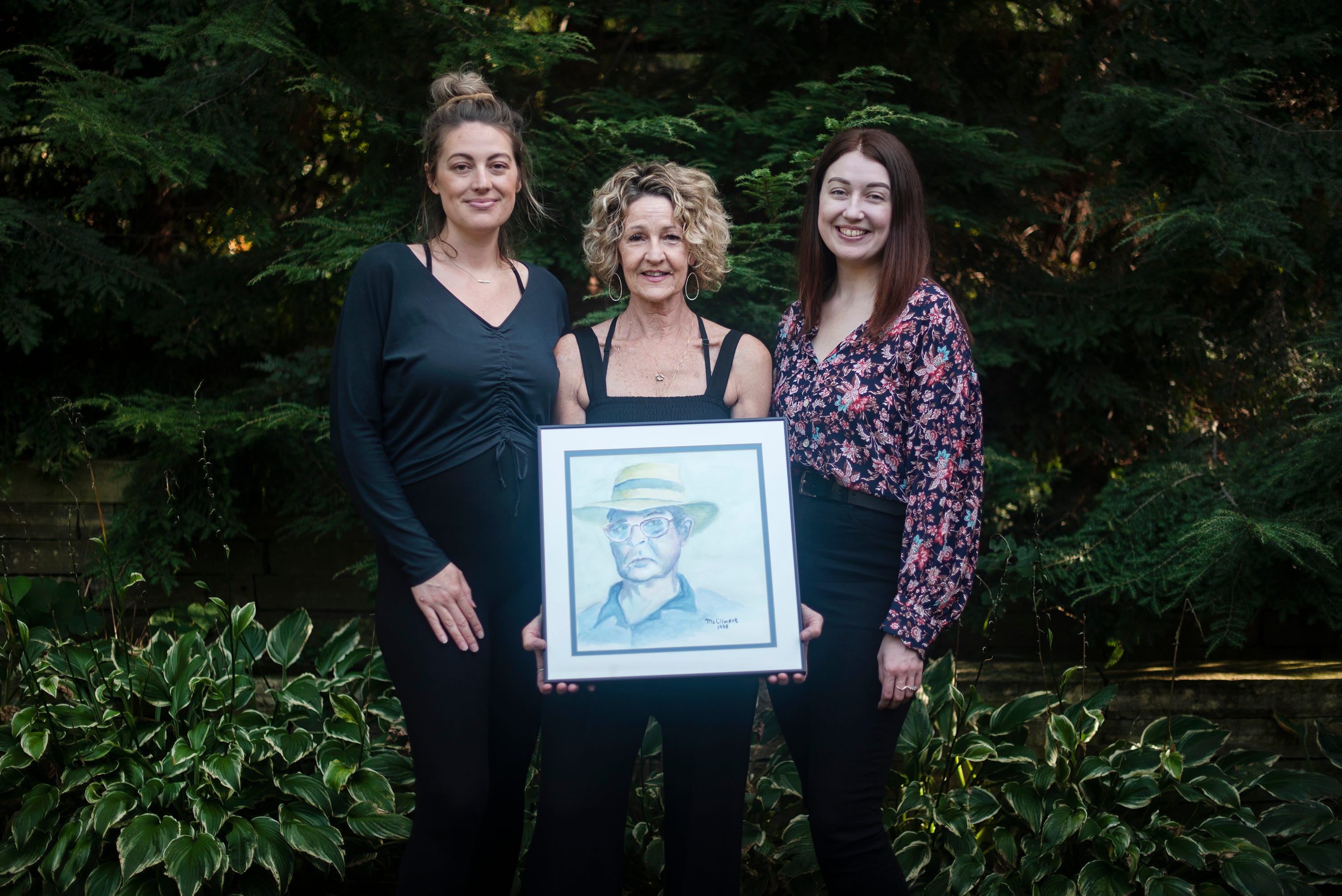 Ed McCliment's daughter Nancy Korpela, center, holding his portrait, and his granddaughters Hannah Landa and Hillary Korpela pose for a photo.
