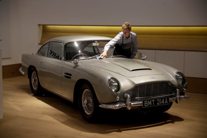 A staff member from the Bonhams motor car department poses for photographers with the 1965 Aston Martin DB5 driven by actor Pierce Brosnan in his role as James Bond in the 1995 movie "GoldenEye" during a photo call at Bonhams auction house in London, Tuesday, June 19, 2018. The car is estimated to fetch between 1.2 million and 1.6 million pounds ($1.6 million to $2.1 million, 1.4 million to 1.8 million euro) in a sale on July 13. (AP Photo/Matt Dunham)