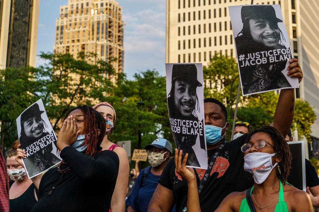 Protesters hold signs outside the Minneapolis 1st Police precinct during a demonstration against police brutality and racism on August 24, 2020 in Minneapolis, Minnesota. - It was the second day of demonstrations in Kenosha after video circulated Sunday showing the shooting of Jacob Blake -- multiple times, in the back, as he tried to get in his car, with his three children watching. (Photo by Kerem Yucel / AFP) (Photo by KEREM YUCEL/AFP via Getty Images)