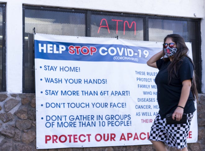 A woman walks into a White Mountain Apache Tribe gas station where a sign indicates practices to help stop the spread of COVID-19.