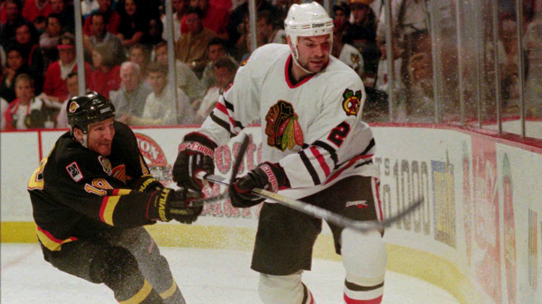 Vancouver Canucks' Tim Hunter, left, checks Chicago Blackhawks' Eric Weinrich as the two battle for the puck during the first period of their second-round playoff game on May 23, 1995, in Chicago.