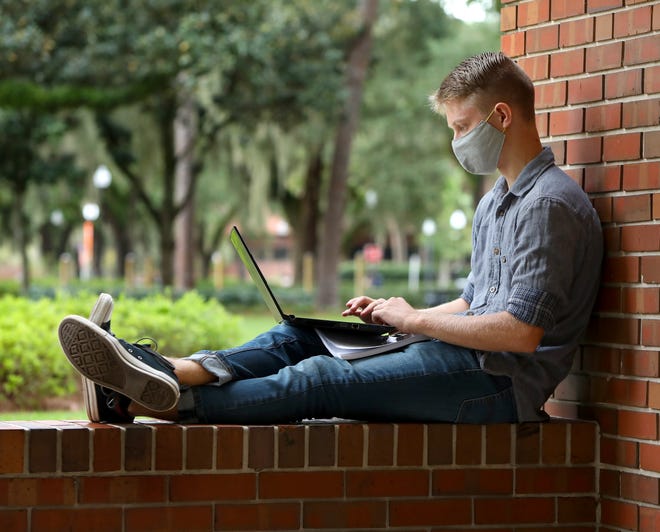 A University of Florida student works on his laptop as he does his online classes while sitting outside of Library West.