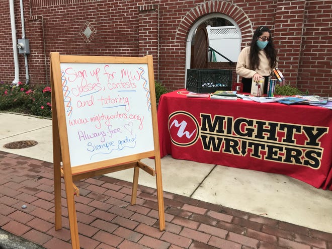 Volunteer Tiffany Veliz sets up a table with free children's books and information about Mighty Writers programs.