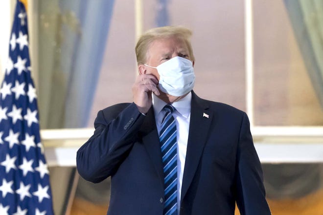 President Donald Trump removes his mask as he stands on the Blue Room Balcony upon returning to the White House Monday, Oct. 5, 2020, in Washington, after leaving Walter Reed National Military Medical Center, in Bethesda, Md. Trump announced he tested positive for COVID-19 on Oct. 2. (AP Photo/Alex Brandon)