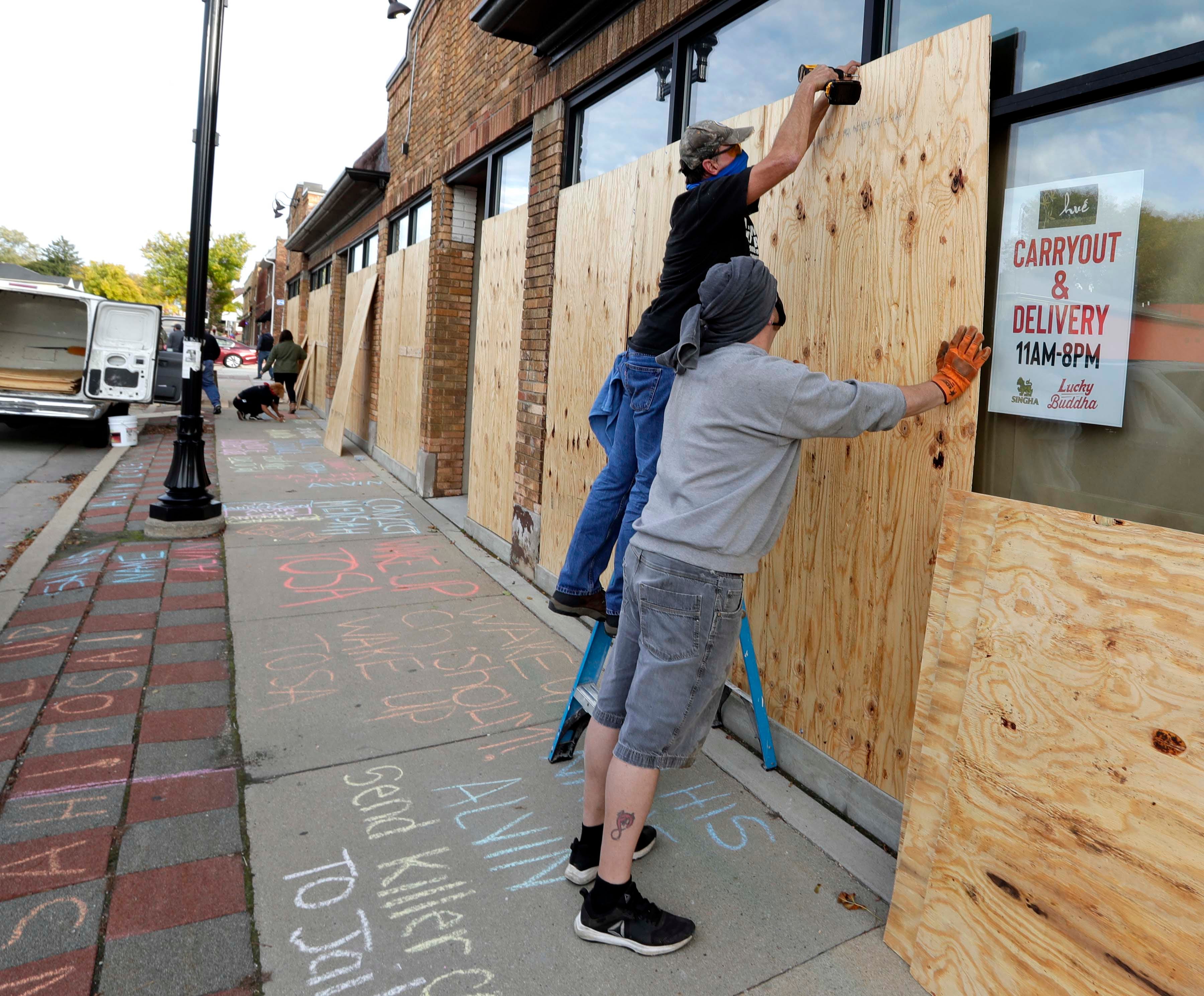 Supporters of Alvin Cole write chalk statements while workers board up businesses near North 65th Street and West North Avenue on Oct. 5, a day before the Milwaukee County District Attorney's Office announced whether Wauwatosa Police Officer Joseph Mensah would face criminal charges in the Feb. 2 fatal shooting of Cole at Mayfair mall.