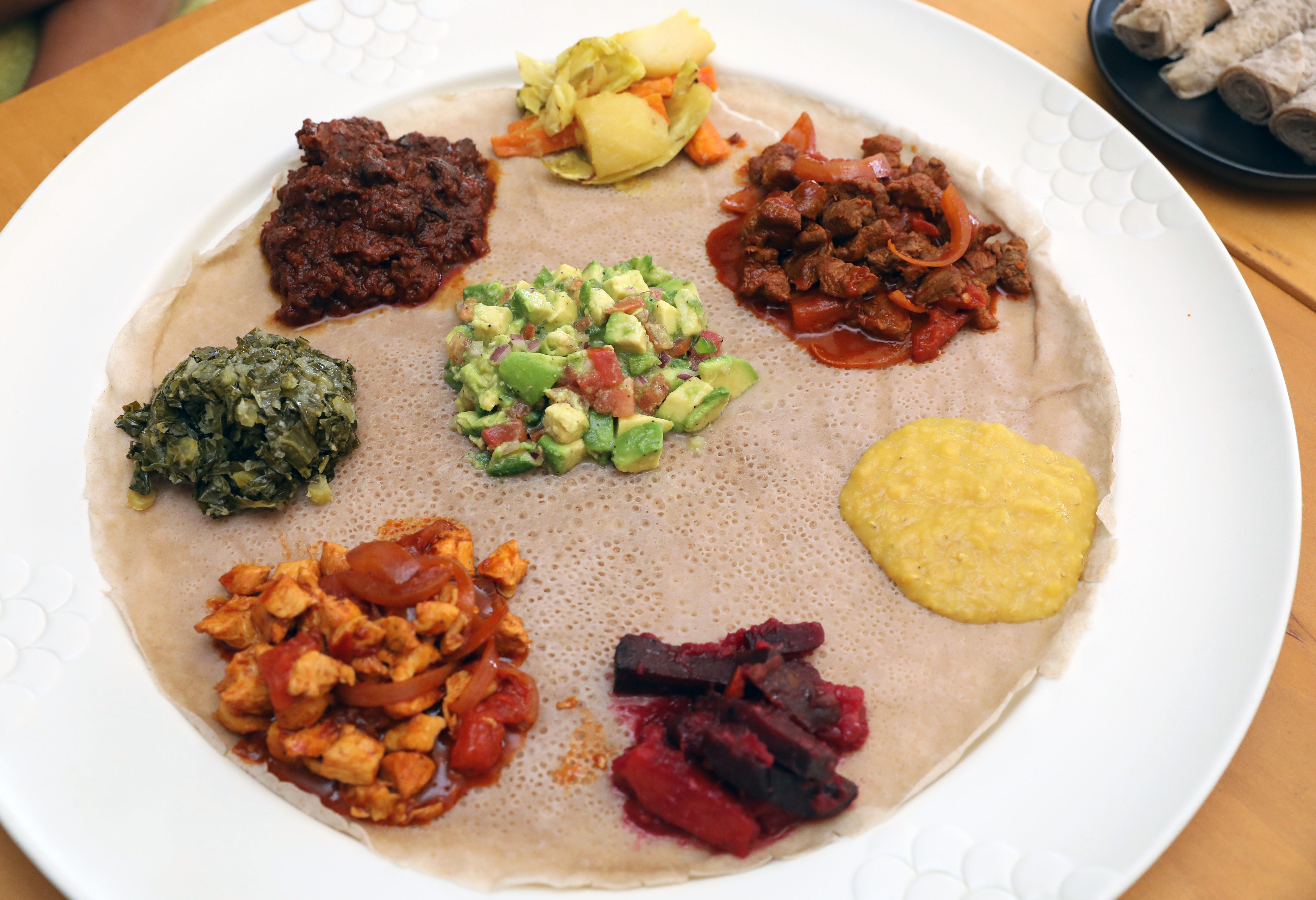 Ethiopian food is served on Injera, a kind of flatbread pancake. Here is a sampling of food from Lalibela Ethiopian Cuisine Restaurant in Mount Kisco, New York. Clockwise from bottom left, doro tibs (chicken); gomen (collard greens); siga wat (slow cooked beef); cabbage; lamb tibs; misir wat alicha (non-spicy split lentils); beets and carrots, and in the center, avocado salad.