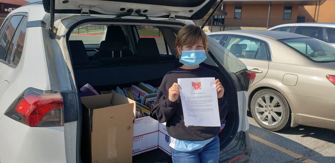 Willa Harvey with a carload full of books to be delivered to local elementary school libraries. Each box contains books for a different school, and she is holding a letter she composed that she presents along with the books.