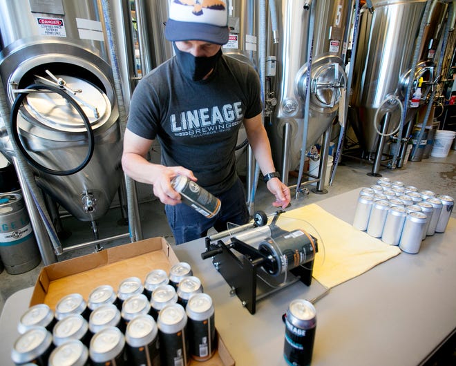 Lineage Brewing co-owner and brewer Carey Hall labels beer cans earlier this month. Lineage, like many breweries, has increased its use of cans since the coronavirus pandemic hit. [Courtney Hergesheimer/Dispatch]