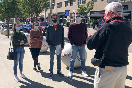 In this Sept. 20, 2020, photo, tour guide John Erardi, right, talks with a tour group on the sidewalk outside the Cincinnati Reds Great American Ball Park in Cincinnati. The walking tour was one of the few groups of people on the street as the Reds and White Sox were inside just an hour before the game without fans because of the pandemic.