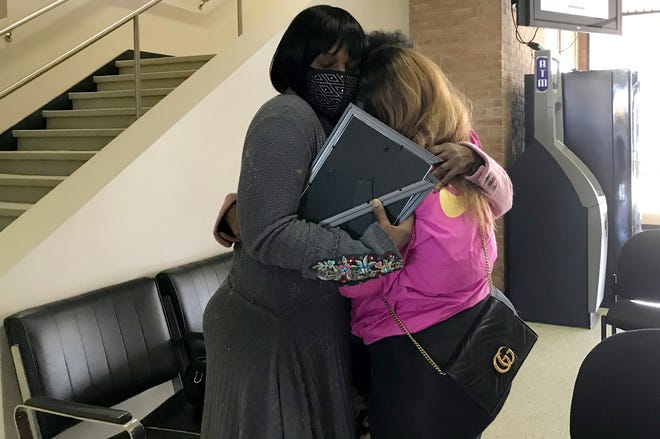Derlanda Farmer, left, of West Bloomfield, holds a photo of her daughter, Isis Rimson, 28, embraces relatives in the lobby during a press conference at Warren police headquarters in which a Bloomfield Hills man was charged in the Oct. 1, 2020 execution-style shooting deaths of three people from Warren.