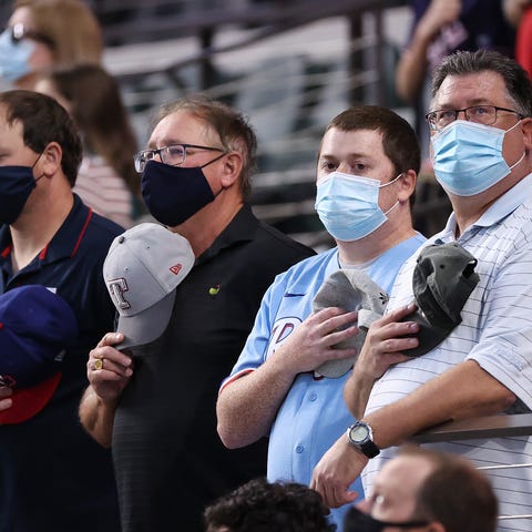 Fans observe the National Anthem as they wear mask