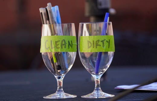 A glass of clean pens stands next to a glass for dirty pens outside a news conference with Colorado governor Jared Polis about the state's spike in cases of the new coronavirus, Oct. 13, 2020, in Denver.