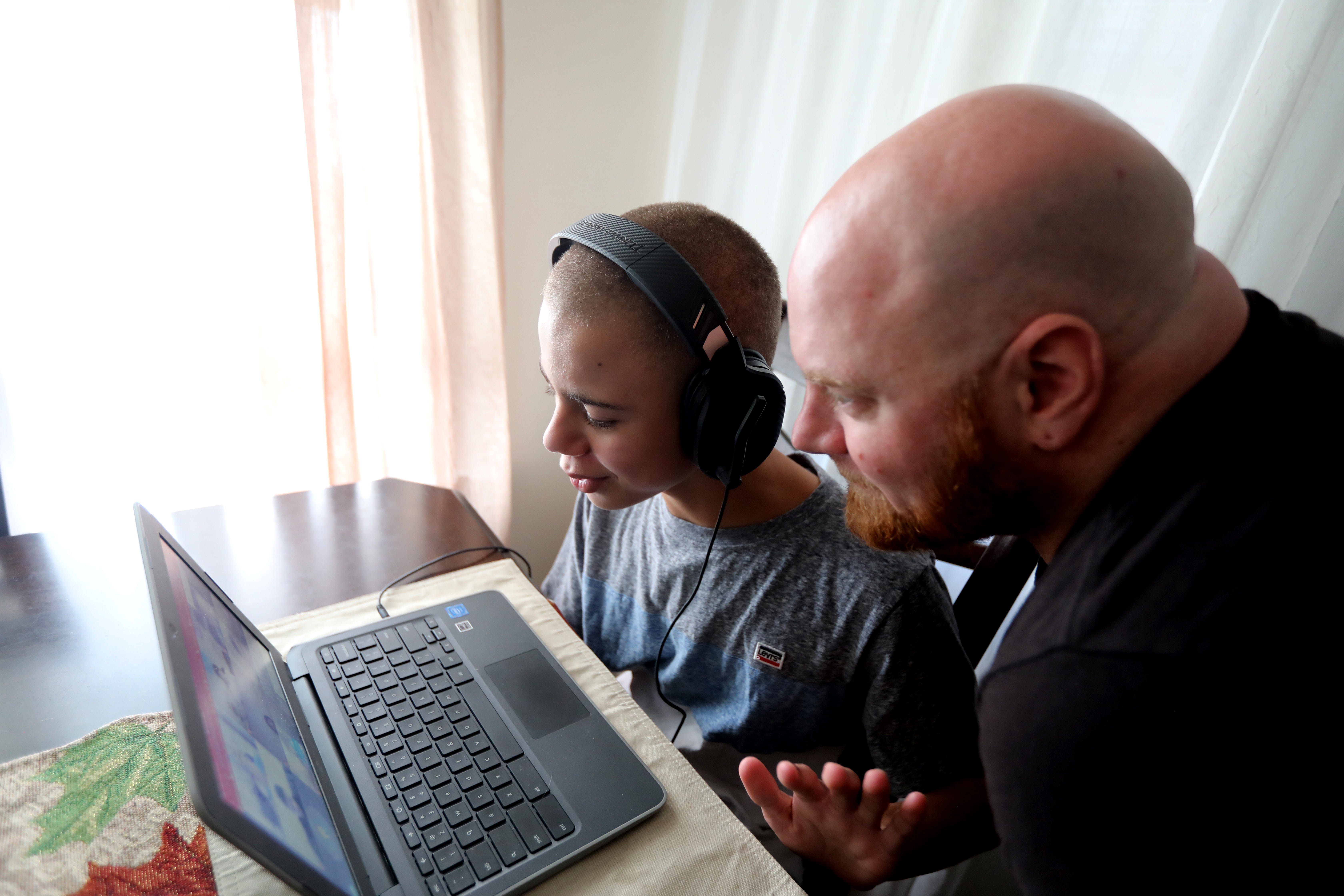 Jordan Jansen, 12, a seventh grader at the Twin Towers Middle School in Middletown, N.Y., takes part in a virtual class while his father Lou looks on Oct. 15, 2020. Jordan, who is autistic, is in a special needs class. His parents say that virtual learning poses special challenges for kids like Jordan with special needs. 