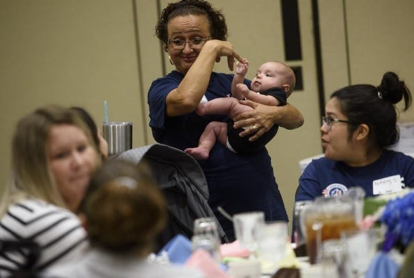 USO volunteer Gigi Warren plays with 4-month-old John Grooms while his mother, Victoria, eats lunch during a baby show for military moms and spouses in August 2019. John's father was on a 15-month deployment.