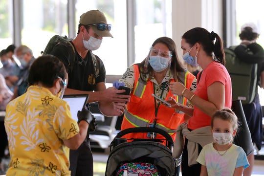 State officials assist visitors at the Daniel K. Inouye International Airport Thursday, Oct. 15, 2020, in Honolulu. A new pre-travel testing program will allow visitors who test negative for COVID-19 to come to Hawaii and avoid two weeks of mandatory quarantine goes into effect Thursday. The pandemic has caused a devastating downturn on Hawaii's tourism-based economy. Coronavirus weary residents and struggling business owners in Hawaii will be watching closely as tourists begin to return to the islands.