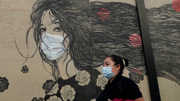 A woman wears a mask while walking past a mural of