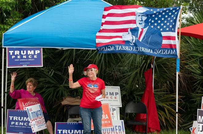 Mercedes Garcia, left and Delia Garcia Mendocal wave at voters outside an early voting site at the Wellington Branch Library in Wellington, Florida on October 21, 2020. (GREG LOVETT / THE PALM BEACH POST)