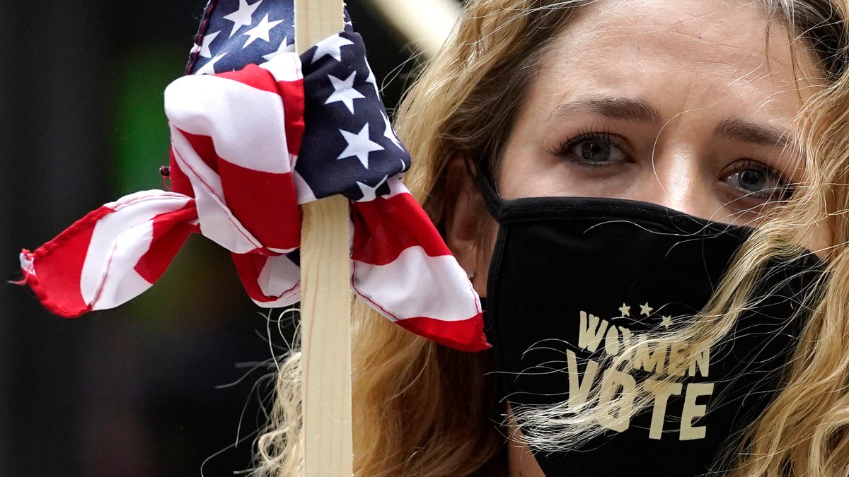 Lindsey Schwartz wears a mask with a message as she holds a sign during the Women's March in downtown Chicago, Saturday, Oct. 17, 2020.