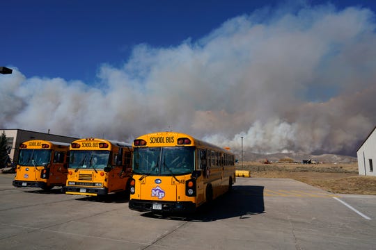 Smoke rises from mountain ridges as a wildfire burns while buses sit idle at the high school Thursday, Oct. 22, in Granby, Colorado.