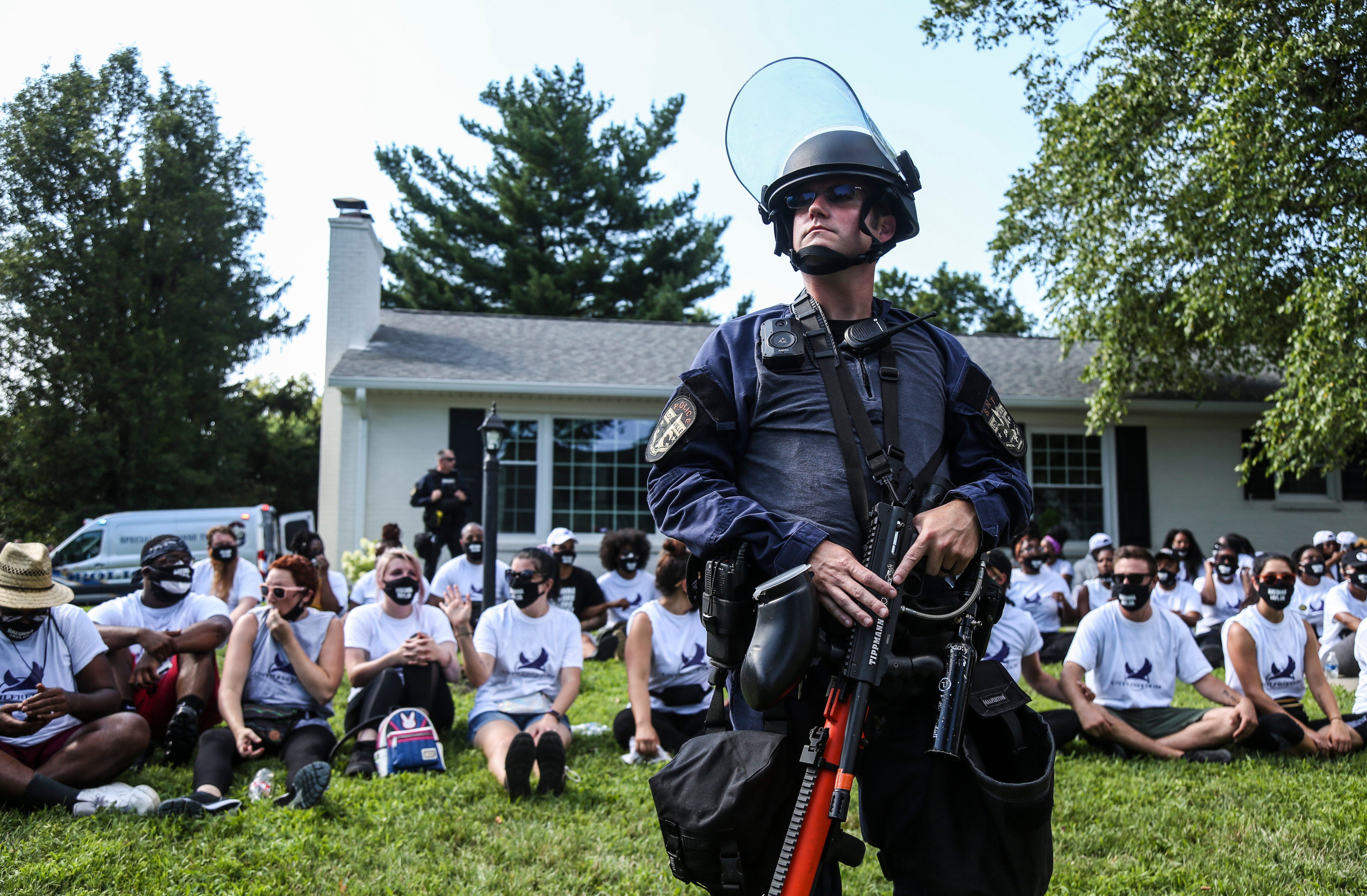 Louisville Metro Police officers stands guard outside the home of Kentucky Attorney General Daniel Cameron as protesters sit in his front yard on July 14, 2020. About two dozen protesters were arrested. They had been chanting Breonna Taylor's name as well as calling for justice after the 26-year-old emergency room technician was fatally shot by police while they were serving a search warrant.