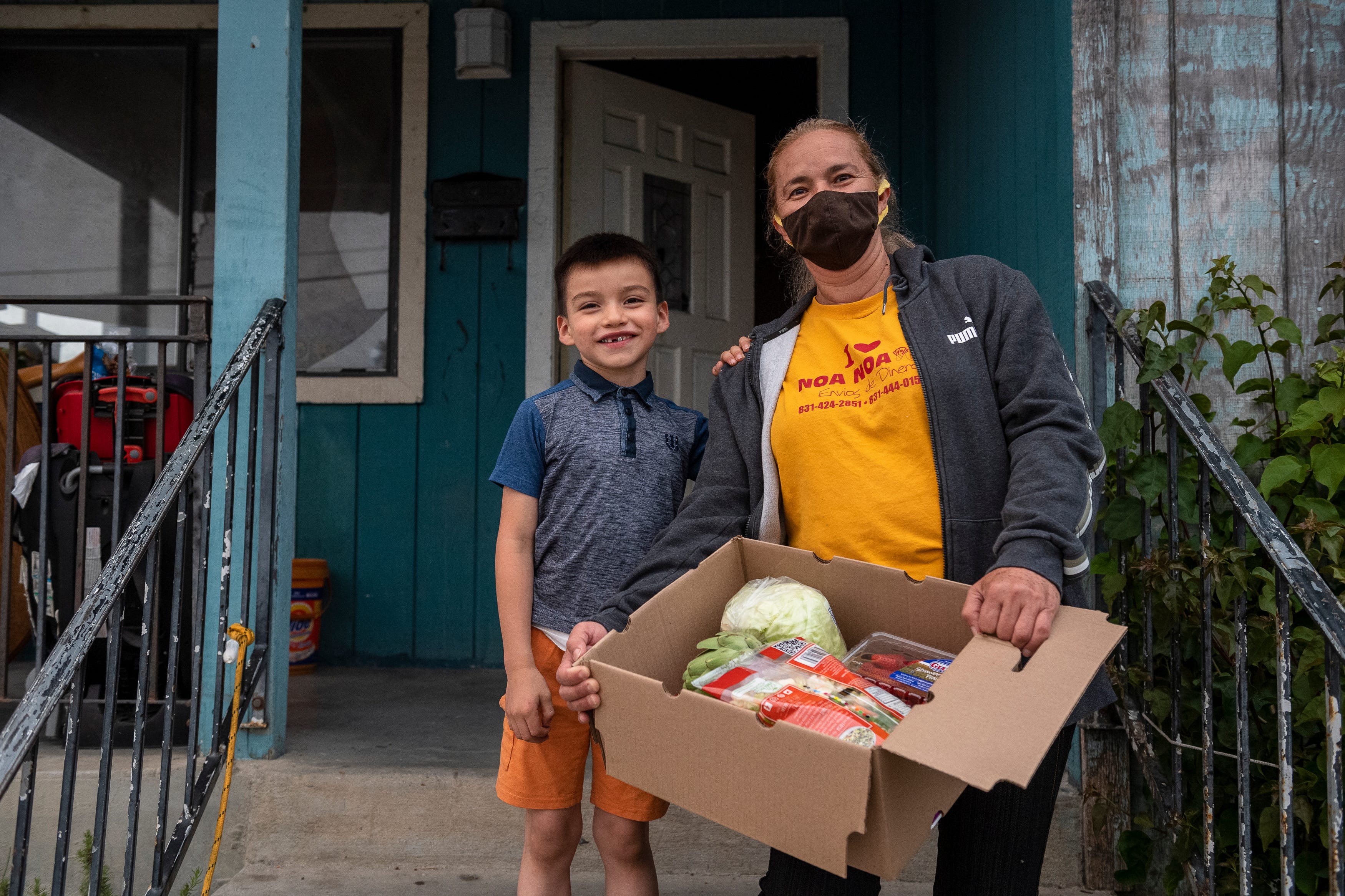 Kender Ricardez Tobon, left, stands on a door step as he rests his left hand on the shoulder of Eufemia "Jenni" Aguilar. She holds a box filled with different vegetables and fruits donated to them by the Future Citizens foundation, Taylor Farms Center for Learning in Salinas, Calif., on Wednesday, Aug.19, 2020. 