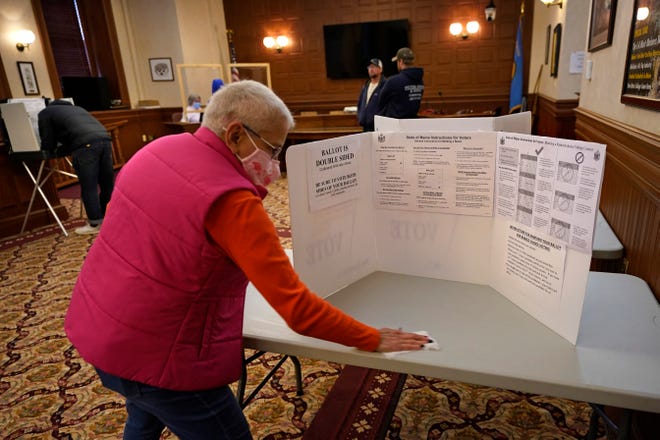 Susan Turcotte, assistant city clerk, disinfects a table after it was used by a resident to fill out an absentee ballot during early voting, Friday, Oct. 30, 2020, in Lewiston, Maine.