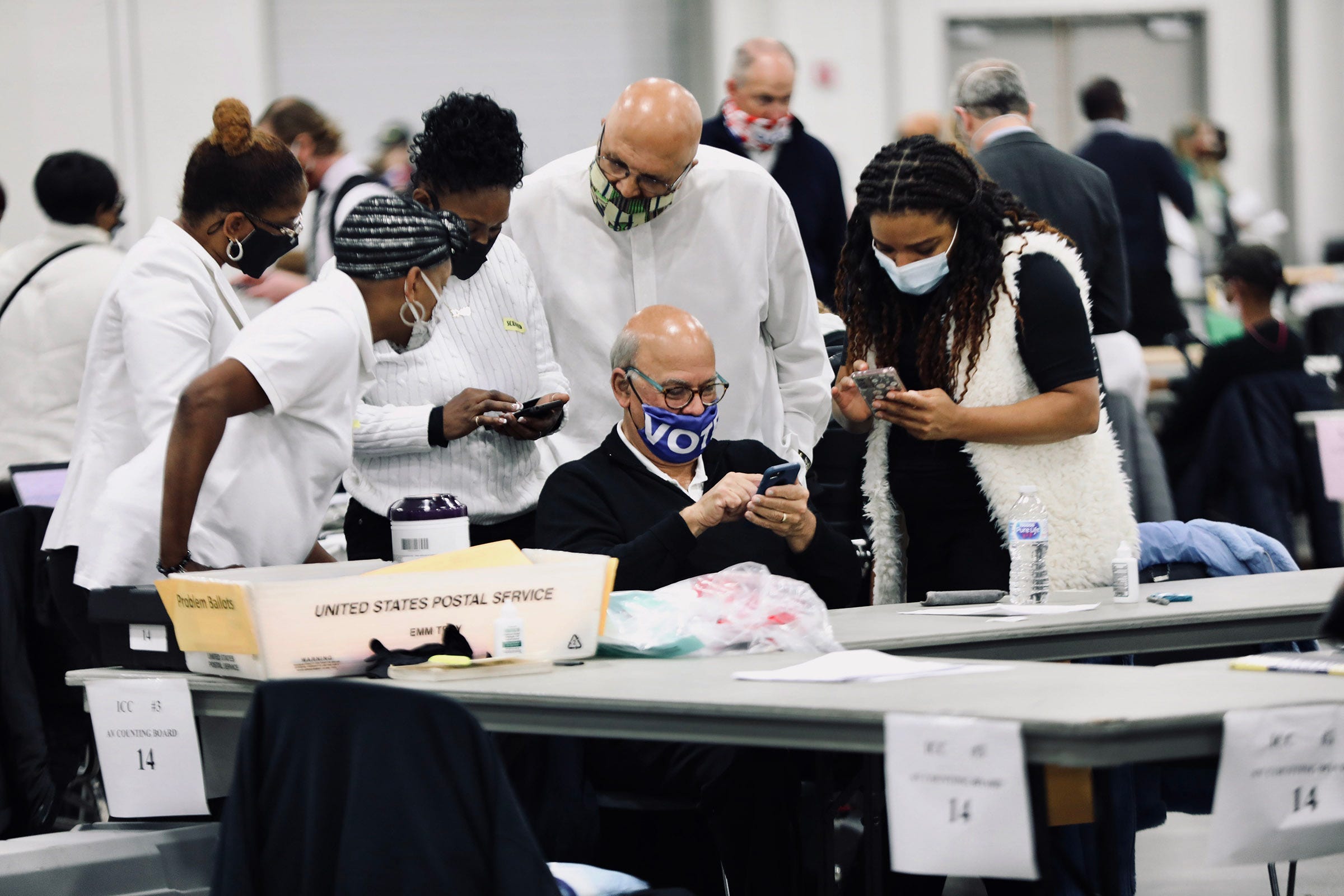 Detroit elections employees examine election results on their phones as they count absentee ballots at the TCF Center on Nov. 4.