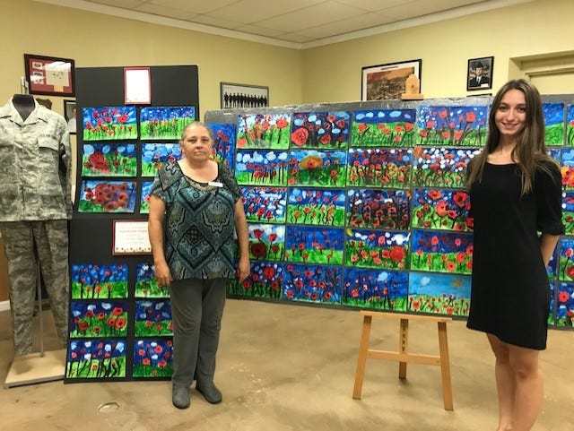 Arendell Parrott Academy art teacher Samantha Rouse, right, poses with Carol Cantu in front of paintings of poppies based on John McCrae's poem "In Flanders Fields" on display at the G.I. Joe's Military Living History Museum, which were painted by 45 first graders in Rouse's class for Veterans Day.