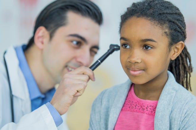 A doctor checks a patient's ear with an otoscope.