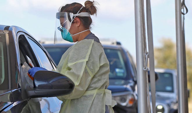 A health care worker at Shannon Clinic North in San Angelo conducts a COVID-19 test at a drive through site Thursday, Nov. 12, 2020.