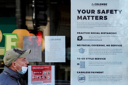 A man walks past a coffee shop with an informational sign about COVID-19 precautions in Chicago on Thursday.