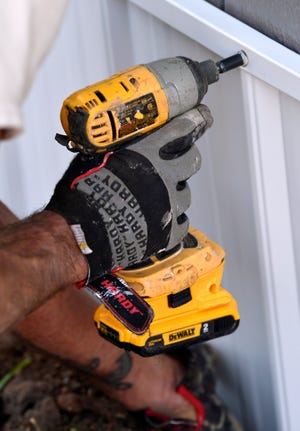 Steve Johnson uses a cordless drill to screw in a section of tin skirt on a north Abilene portable building for the Honey Do general contractors.