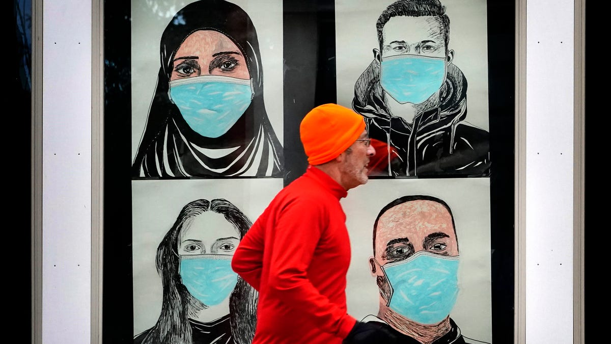 In this Nov. 16, 2020, file photo, a runner passes by a window displaying portraits of people wearing face coverings to help prevent the spread of the coronavirus in Lewiston, Maine. An executive order by Gov. Janet Mills' requires Maine citizens to wear face coverings in public settings, regardless of the ability to maintain physical distance.