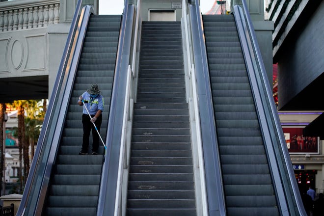 A worker cleans an escalator along the Las Vegas Strip, Thursday, Nov. 19, 2020, in Las Vegas. As the coronavirus surges to record levels in Nevada, the governor has implored residents to stay home. But Democrat Steve Sisolak has also encouraged out-of-state visitors, the lifeblood of Nevada's limping economy, to come to his state and spend money in Las Vegas.