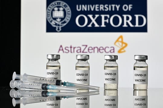 Vials with COVID-19 vaccine stickers attached and syringes are pictured in front of University of Oxford and AstraZeneca logos.