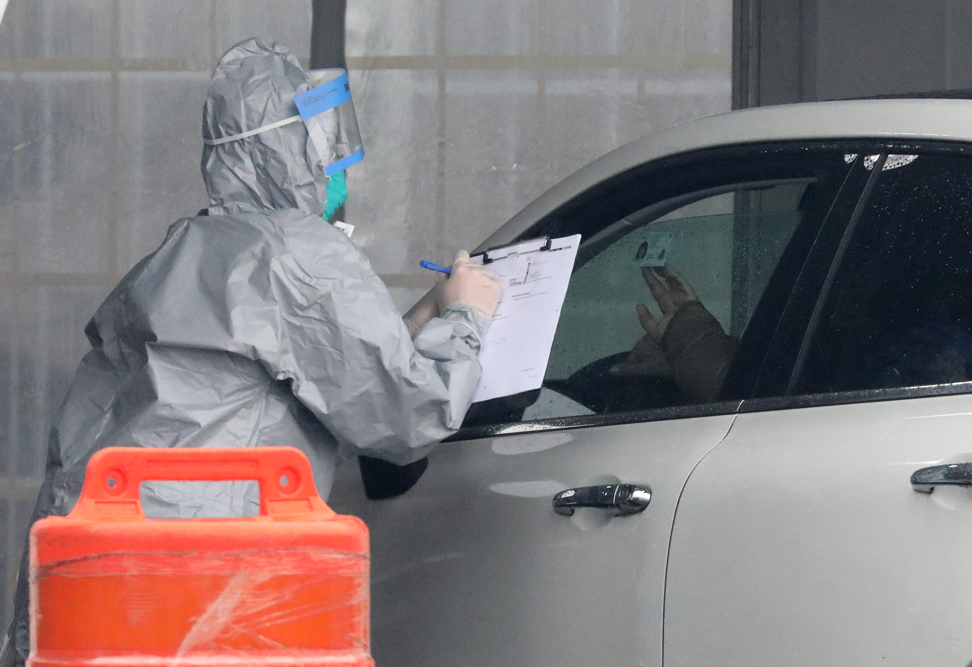 A person holds up their ID as a worker in protective clothing gathers information from people that want to get tested, at Glen Island Park in New Rochelle, as New York State's first drive through COVID-19 mobile testing center opens, March 13, 2020.