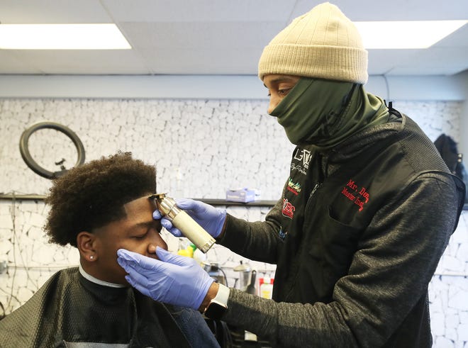 Rodney Dennis, owner of Levels Barber Studio, cuts the hair of Aaron Nance, 21, at his downtown Akron barbershop. (State rules allow customers to remove their masks when they sit down to have hair, beards and sideburns trimmed.) Dennis has convinced hundreds of customers to fill out voter registration forms at his barber shops. But since 2016, he says the young Black men in his barber’s chair have increasingly expressed a complete lack of confidence in the democratic process.