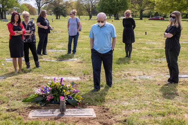 Oliver Wilding, center, stands at the tombstone of his mother, Barbara Wilding, in April 2020. Wilding died from COVID-19 at the age of 81. Family members watched her burial from their vehicles and afterward, gathering at the grave, they followed social distancing restrictions.